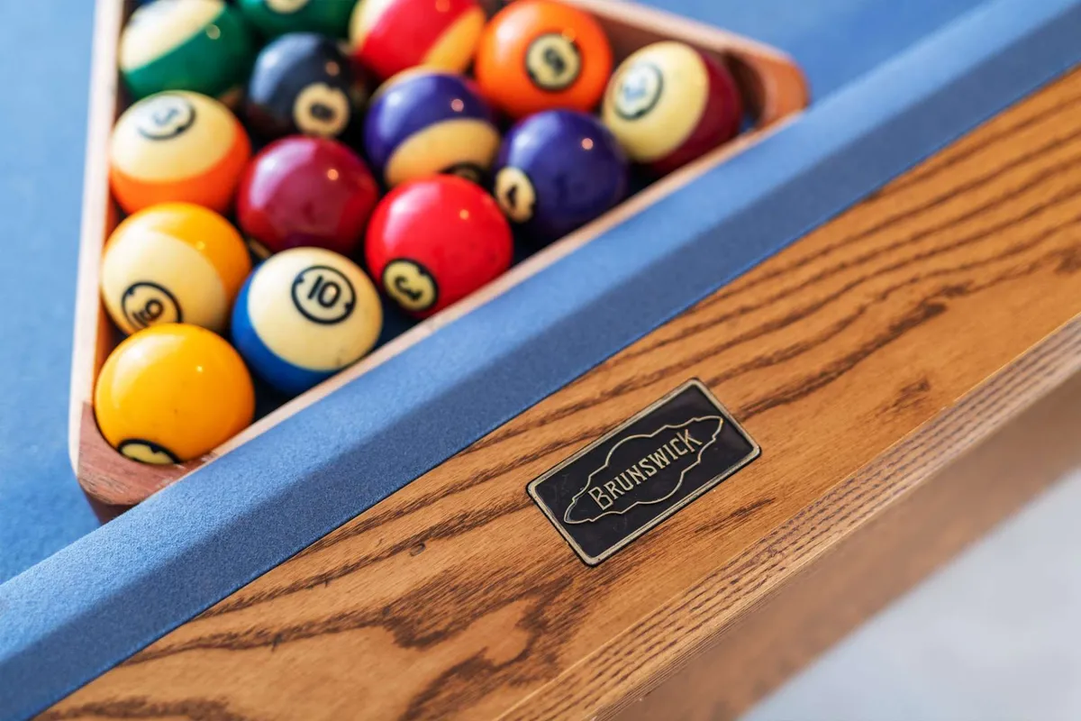 An inviting interior view of a game room featuring a pool table with a triangle of billiard balls and the Brunswick logo. The scene is lively and casual, emphasizing social activities and fun family time at home.