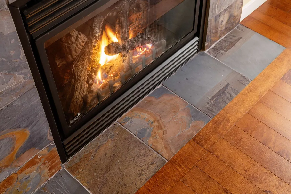 A warm, inviting room centered around a glowing fireplace with stone tiles, ideal for gathering, reading by the fire, or relaxing. The ambiance is cozy, suggesting comfort after time spent outdoors.