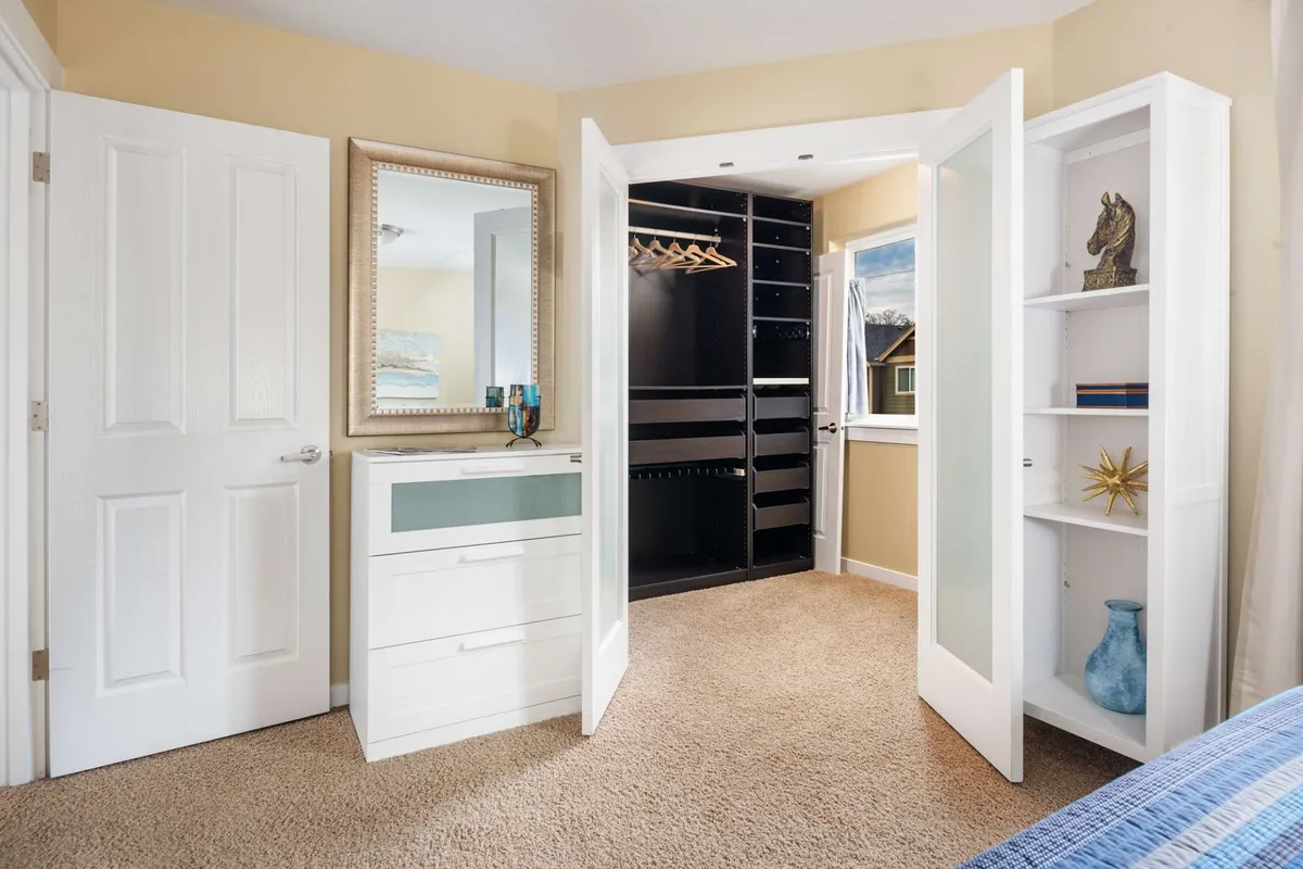 A functional dressing and storage area featuring a dresser, closet space, mirror, and bookshelf. The room feels calm and organized, supporting both morning routines and evening wind-downs.