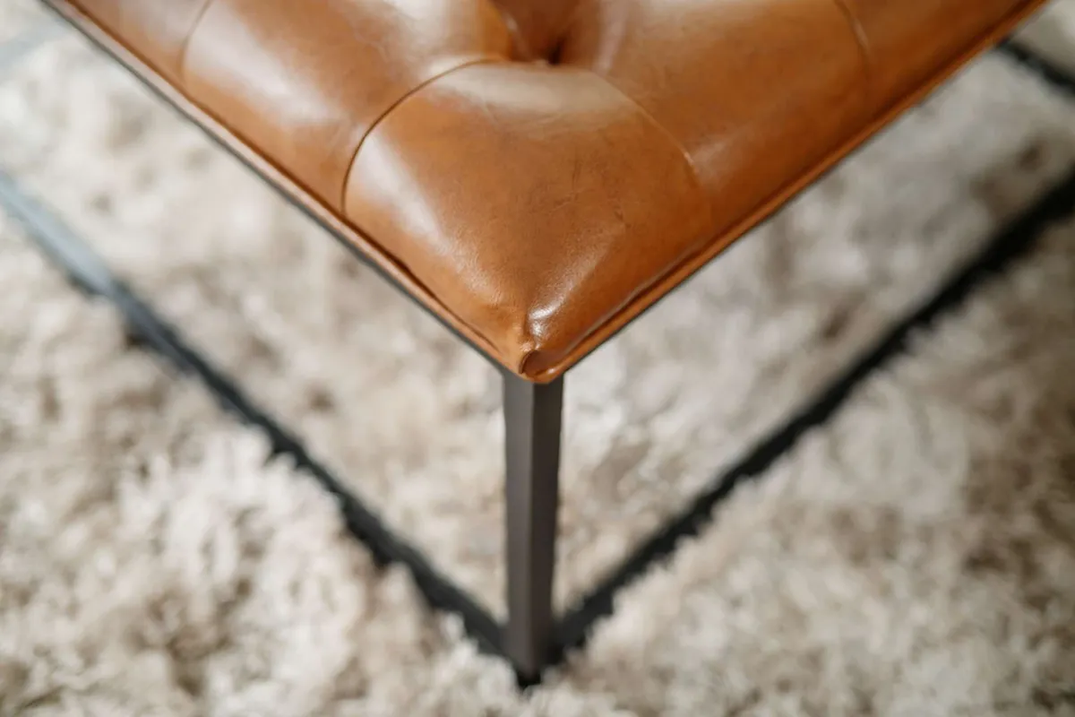A cozy living area featuring a leather ottoman atop a textured rug, arranged for relaxing, reading, or socializing. The space is bright and inviting, with decor and layout conducive to unwinding after a day out.