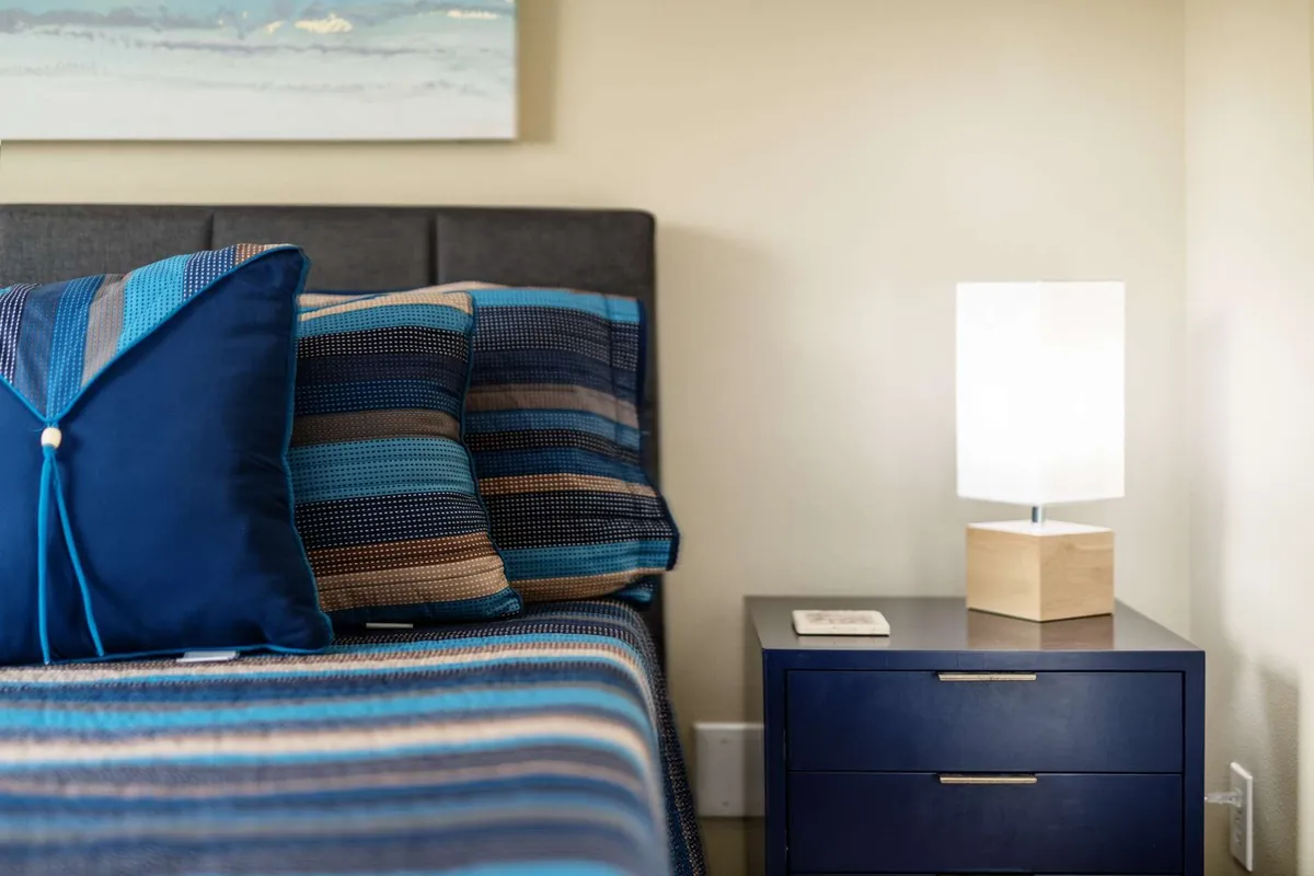 A peaceful bedroom scene with a bed dressed in striped bedding, decorative pillows, and a nightstand with a lamp, creating a tranquil, restful atmosphere.