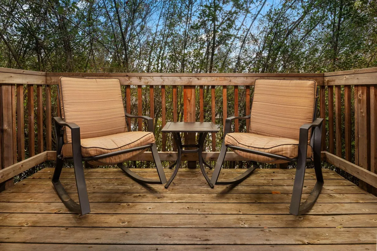 An exterior balcony scene with two rocking chairs and a small table, framed by lush greenery. The tranquil outdoor setting invites morning coffees or sunset toasts.