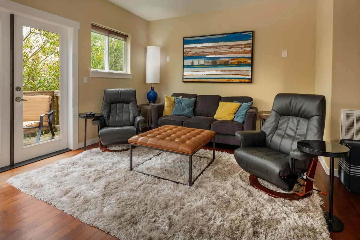 A calm, welcoming living area with plush seating, a coffee table, and a large window offering greenery views. The setting feels peaceful, comfortable, and ideal for relaxing with a pet or unwinding after work.