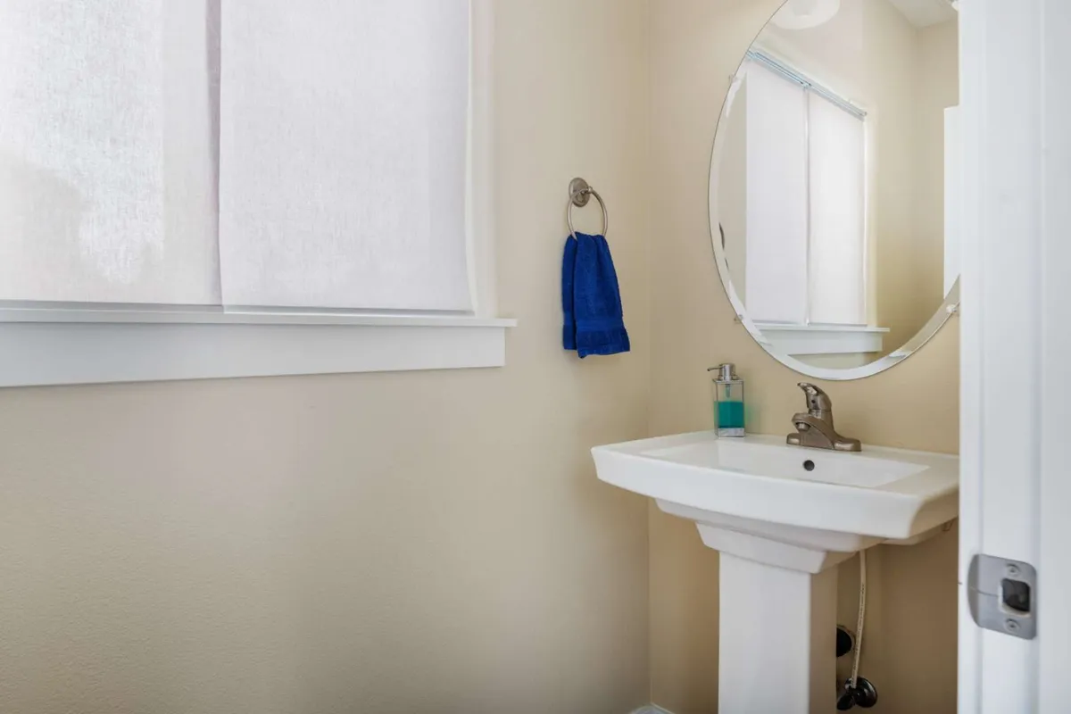 A serene bathroom with a bright sink area, a large mirror, and a blue towel for a pop of color. The setting is inviting, ideal for personal grooming or unwinding after a long day.