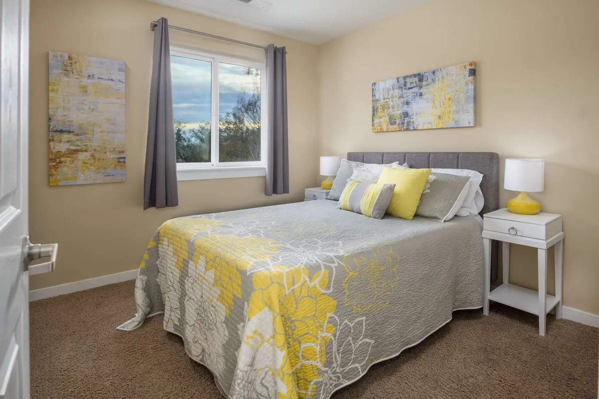 A bright, cheerful bedroom featuring a bed with yellow accents, artwork adorning the walls, and a window that lets in ample natural light. The space feels airy and inviting, ideal for restful nights or enjoying a peaceful morning.